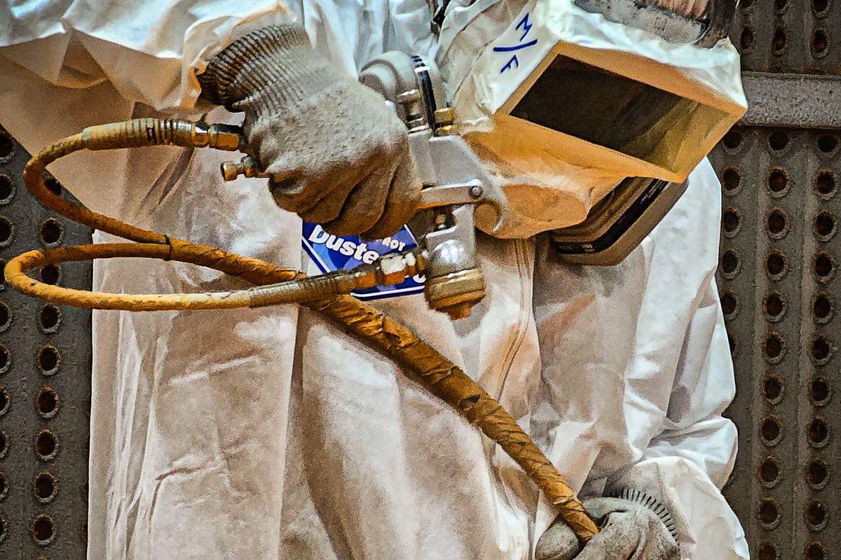 Arbeiter in Schutzanzug beim Strahlen einer Metalloberfläche