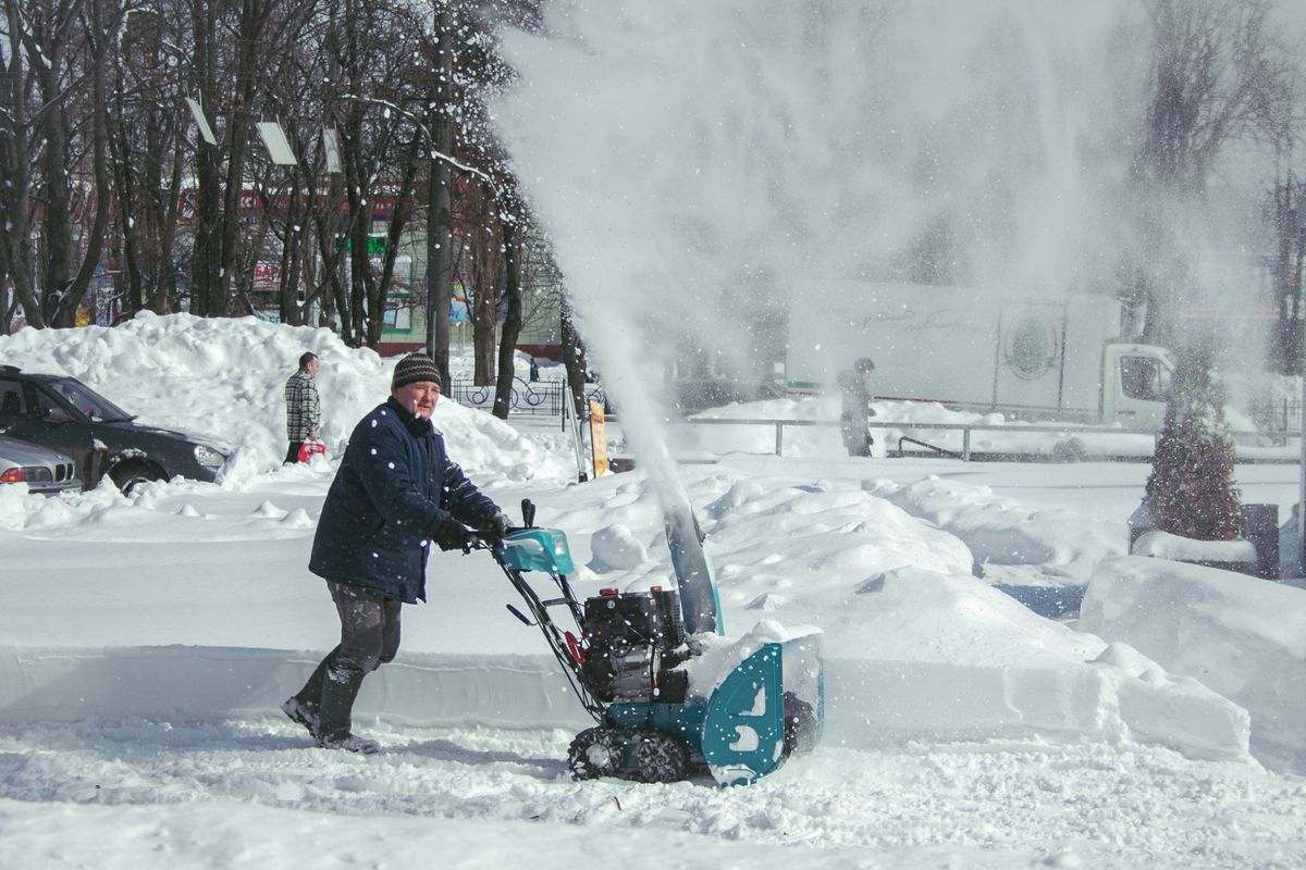 Mitarbeiter räumt mit einer Schneefräse einen Weg vor einem Gebäude